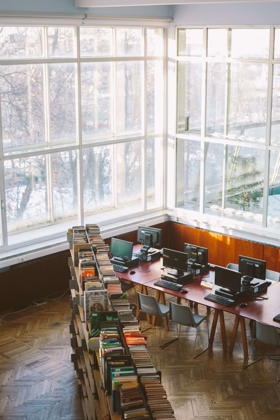 Long study desks lined with computers beside tall library windows